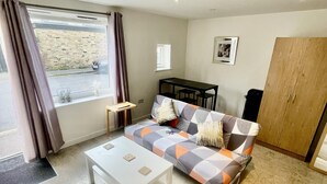 A modern living room with a sofa, a coffee table, a wooden cabinet, and a window with curtains. - Beautiful Studio in Cambridge City Centre (Cambridge)