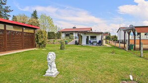 A residential property with a well-maintained lawn, a stone lion statue, and a house with a red roof and a covered patio area. - Ferienhaus Waren (Müritz) (Waren (Müritz) OT Ware)
