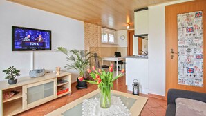 A living room with a television, a small table with a vase of flowers, a bookshelf, and a door with a welcome poster. - Ferienhaus Waren (Müritz) (Waren (Müritz) OT Ware)