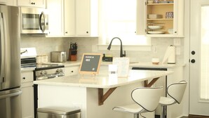 A modern kitchen with stainless steel appliances, a central island with bar stools, and a welcome sign.