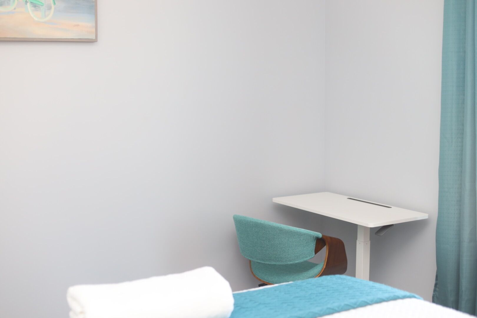 A hotel room with a bed, a chair, a small table, and a painting on the wall.