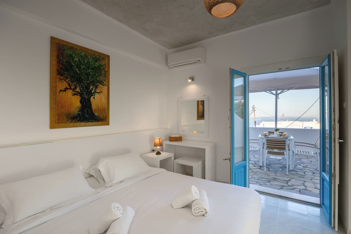A hotel room with a bed, a desk, a painting, and a balcony with a table and chairs.