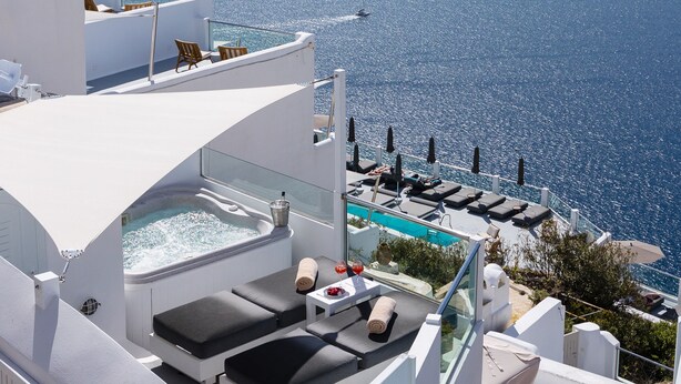A rooftop pool area with lounge chairs and a hot tub, overlooking a scenic ocean view. - Nevma Suites (Santorini)