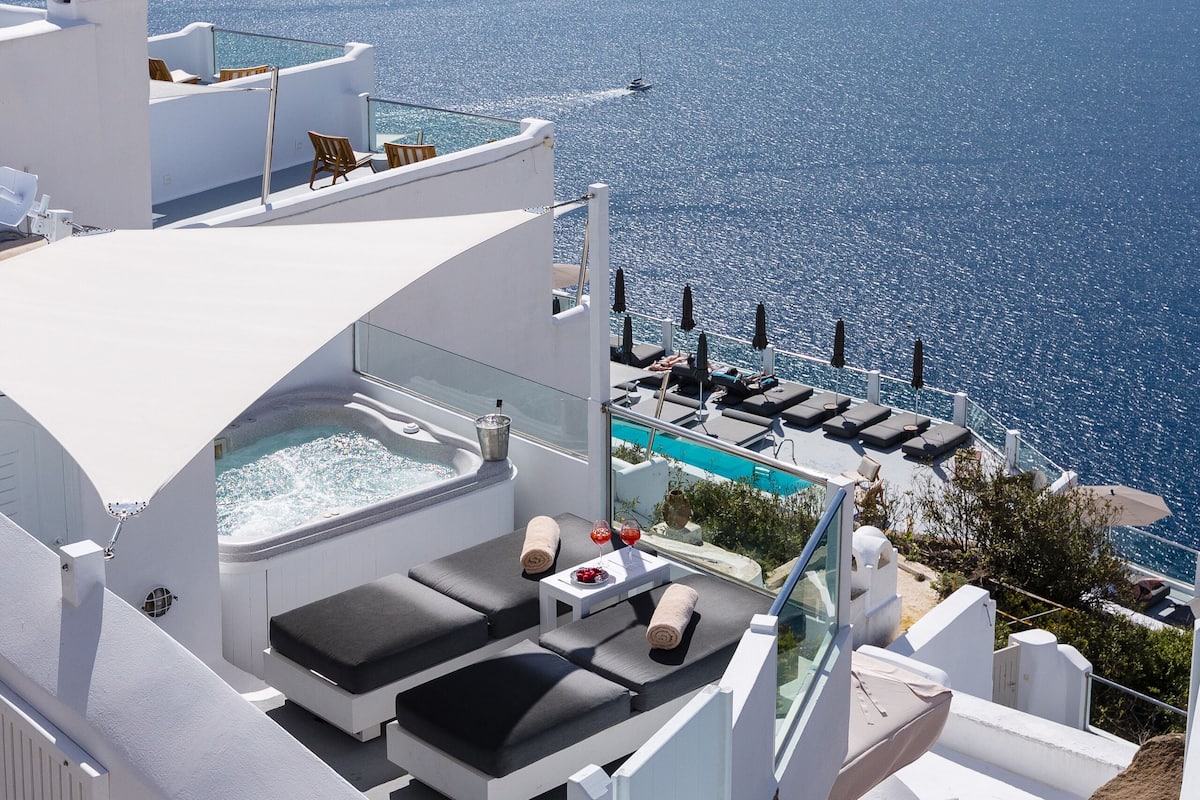 A rooftop pool area with lounge chairs and a hot tub, overlooking a scenic ocean view.