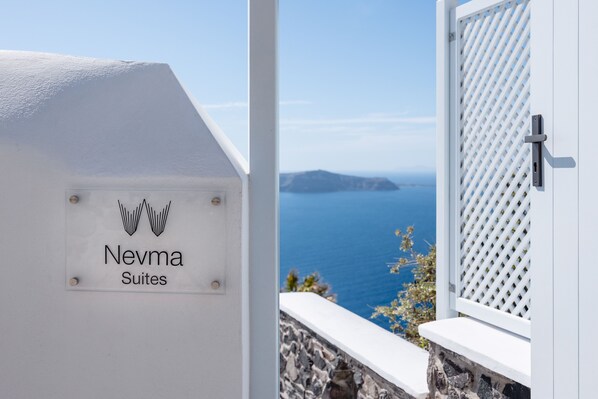 Señal de Nevma Suites con vista al mar y una ventana con celosía blanca.