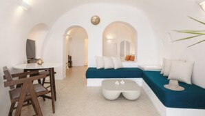 A modern living room with a sofa, a coffee table, and a dining table with chairs. - Nevma Suites (Santorini)