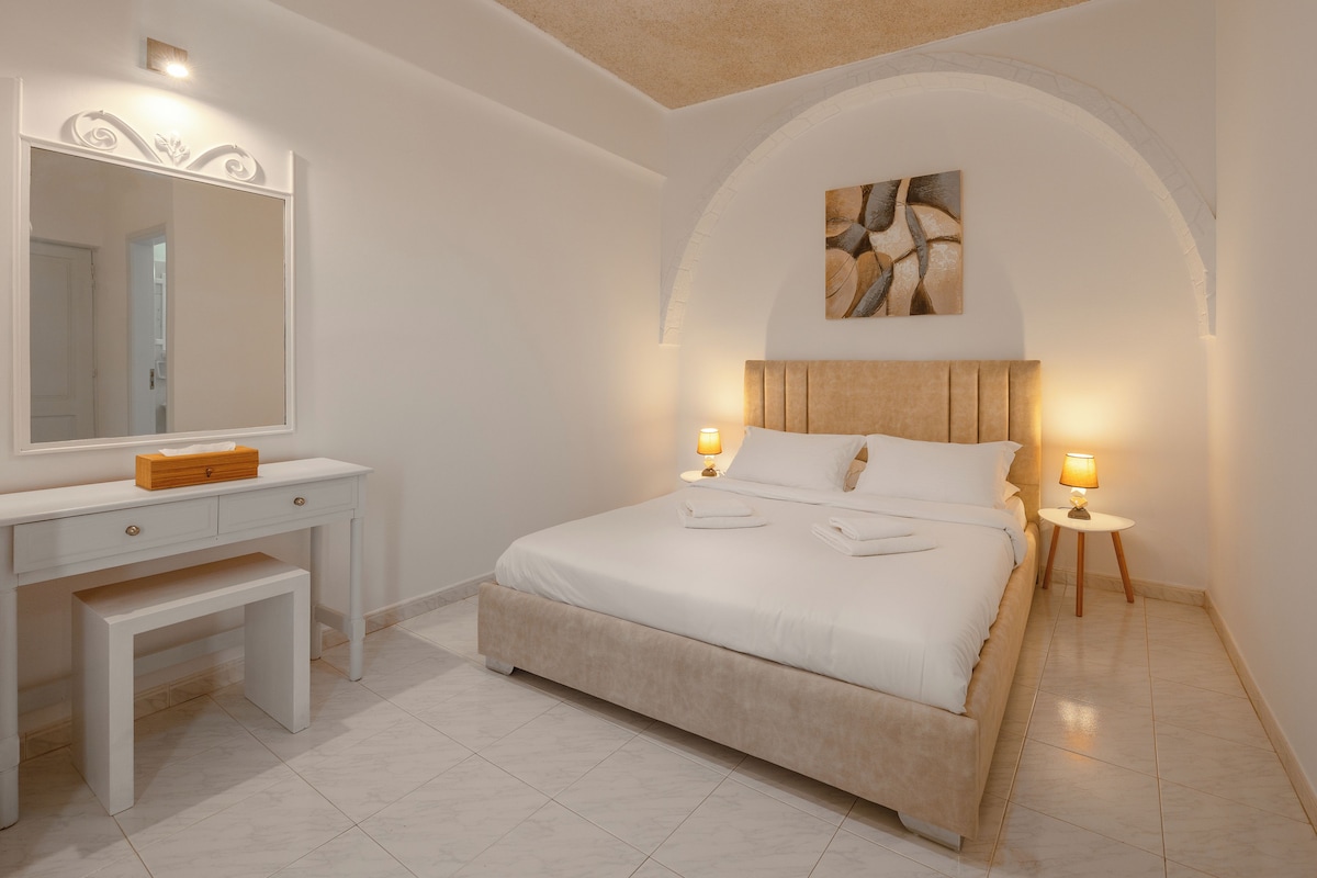 A bedroom with a bed, bedside tables, a mirror, and a bench.