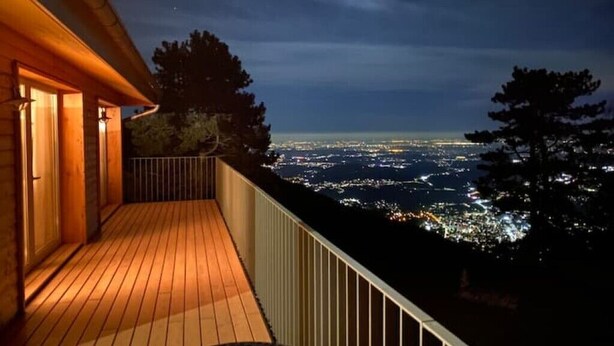 A wooden deck with a railing overlooking a cityscape at night. - Studio on Monte Generoso (Castel San Pietro)