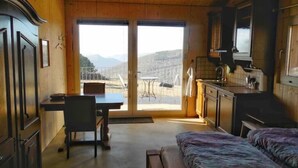 A cozy room with a bed, a desk, and a view of mountains through a sliding door. - Studio on Monte Generoso (Castel San Pietro)