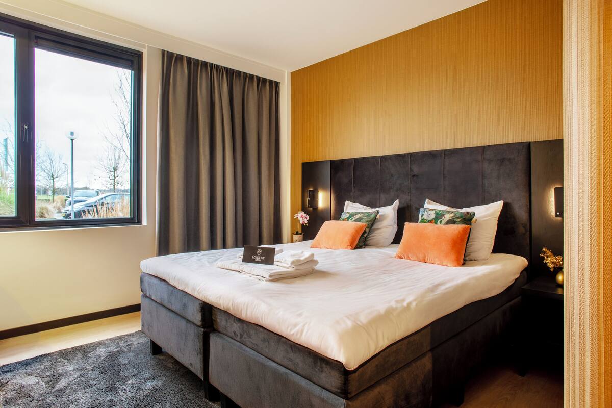 Une chambre d’hôtel moderne, dotée d’un grand lit, d’une table de chevet, d’une fenêtre avec des rideaux et offrant une vue sur l’extérieur.