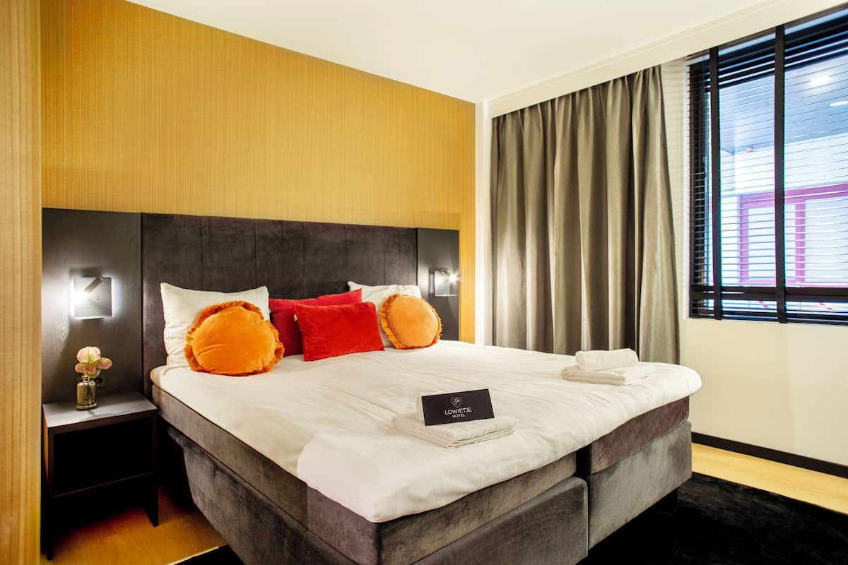 Une chambre d’hôtel moderne avec un grand lit, une table de chevet et une fenêtre avec des rideaux.