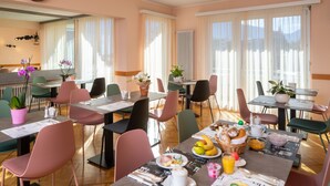 A dining area with multiple tables and chairs, breakfast items, and potted plants.