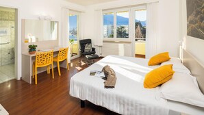 A hotel room with a bed, a desk, a chair, a window with a view of buildings, and a bathroom.
