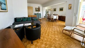 A modern living room with a sofa, a dining table, and chairs. There is a kitchen area in the background.