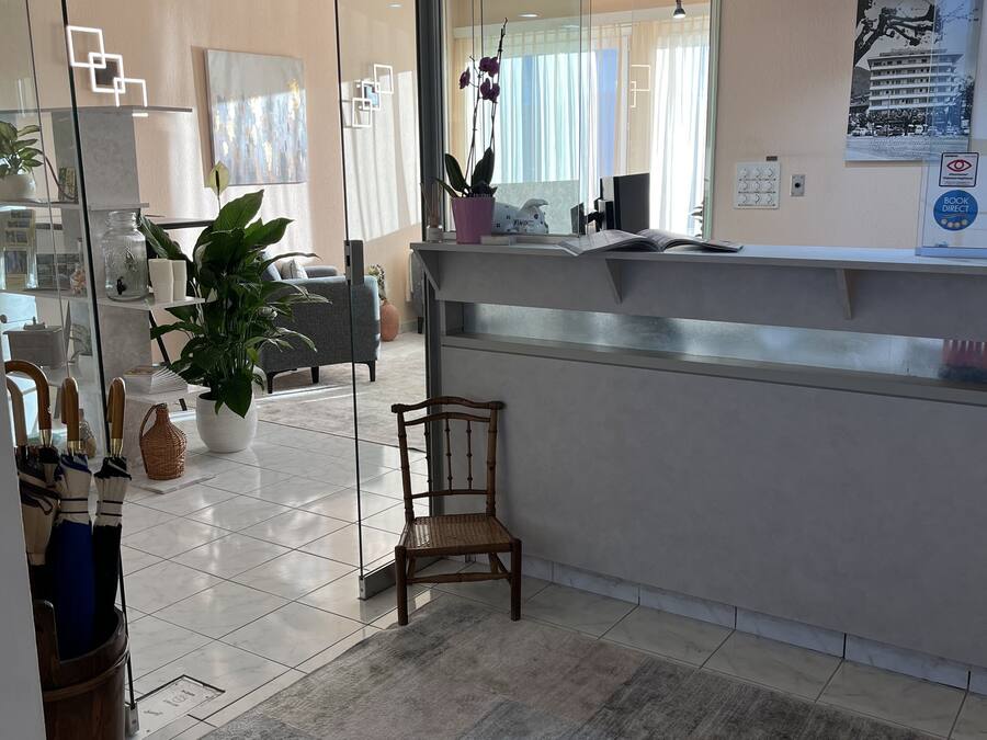 A modern hotel lobby with a reception desk, seating area, and a large window with curtains.