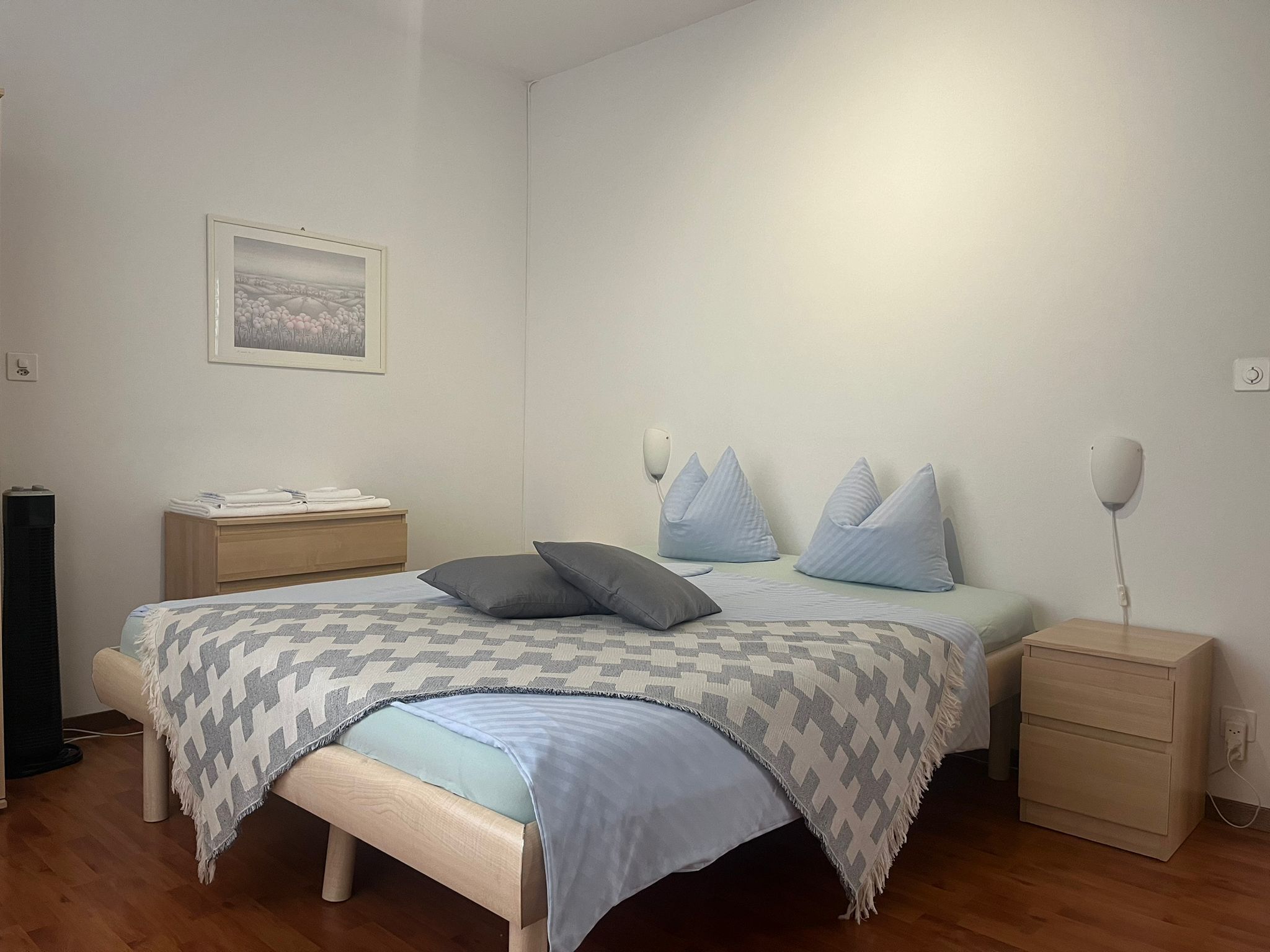 A bedroom with a bed, bedside tables, a nightstand, a lamp, and a framed picture on the wall.