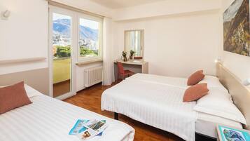 Ein Hotelzimmer mit zwei Betten, einem Schreibtisch und Blick auf eine gebirgige Landschaft.