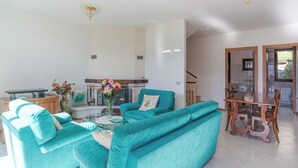 A spacious living room with teal sofas, a wooden dining table, and a kitchen area in the background. - Lenno Glamour (Tremezzina)