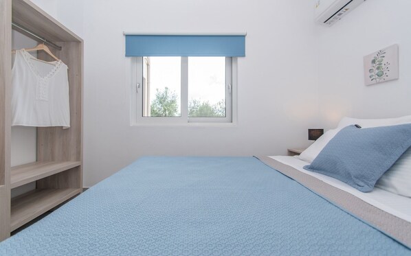 A bedroom with a bed, a wardrobe, a window with a blue blind, and a wall-mounted air conditioner.