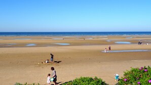 Ein weiter Sandstrand mit Wasserläufen, blauem Himmel und weiter Meereslandschaft.