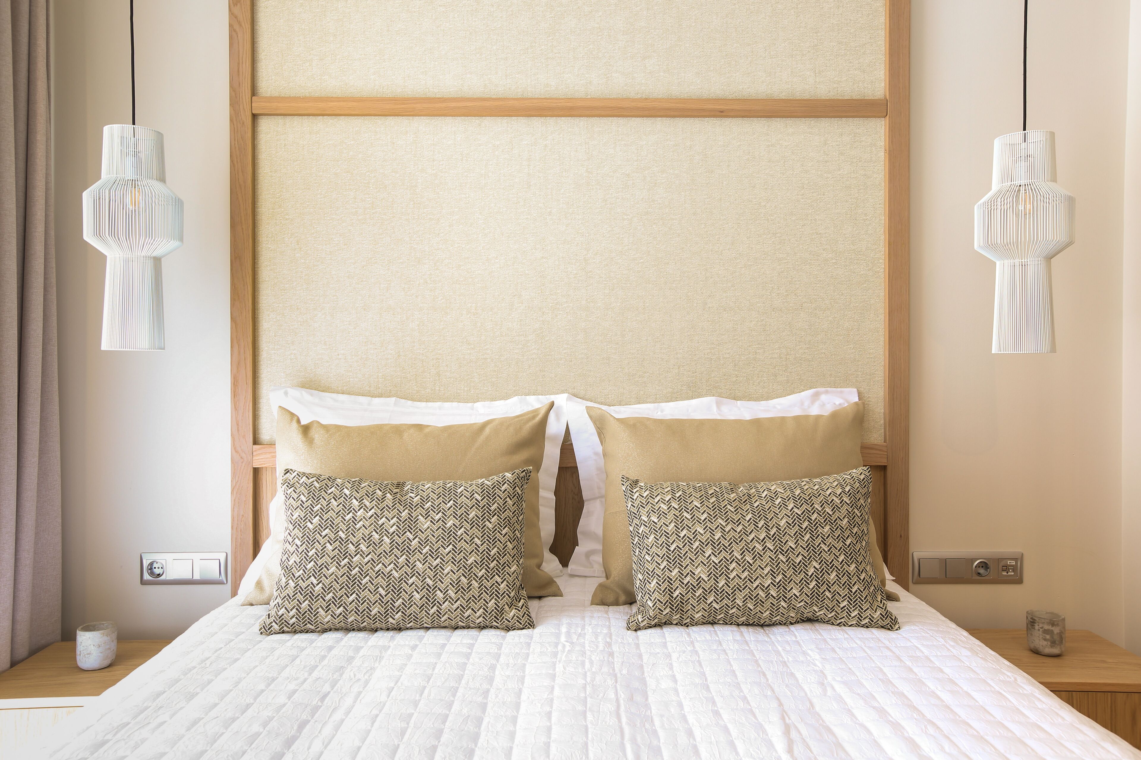 Una cama bien hecha con dos almohadas estampadas, un cabecero de madera y dos lámparas colgantes.