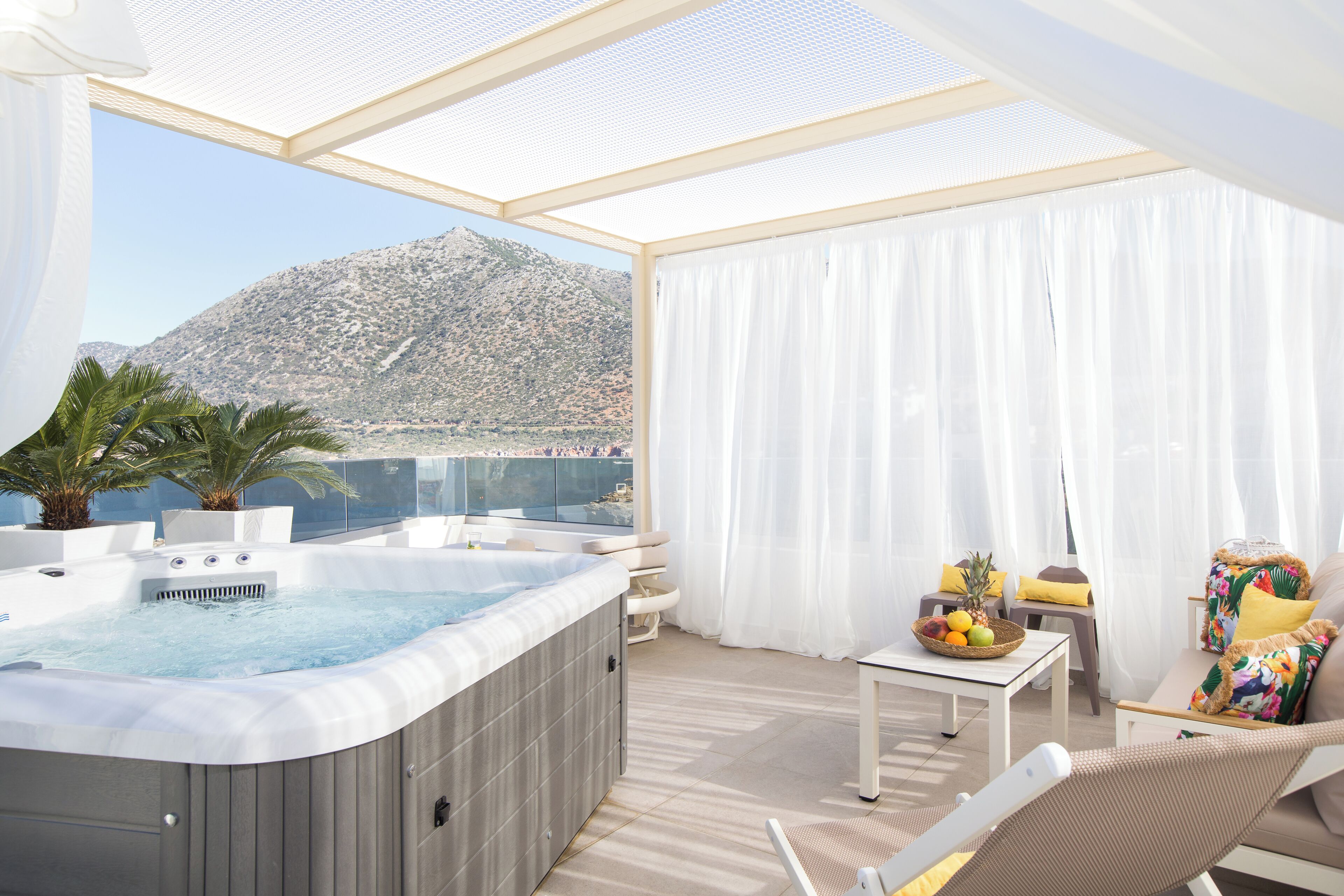A balcony with a hot tub, a table with fruit, and a view of a mountain.