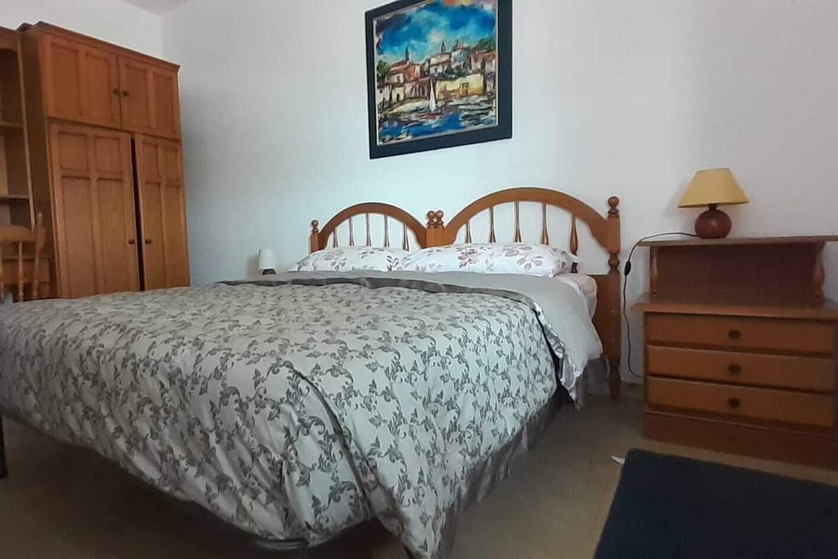 A bedroom with a bed, a wooden wardrobe, a desk, and a lamp.