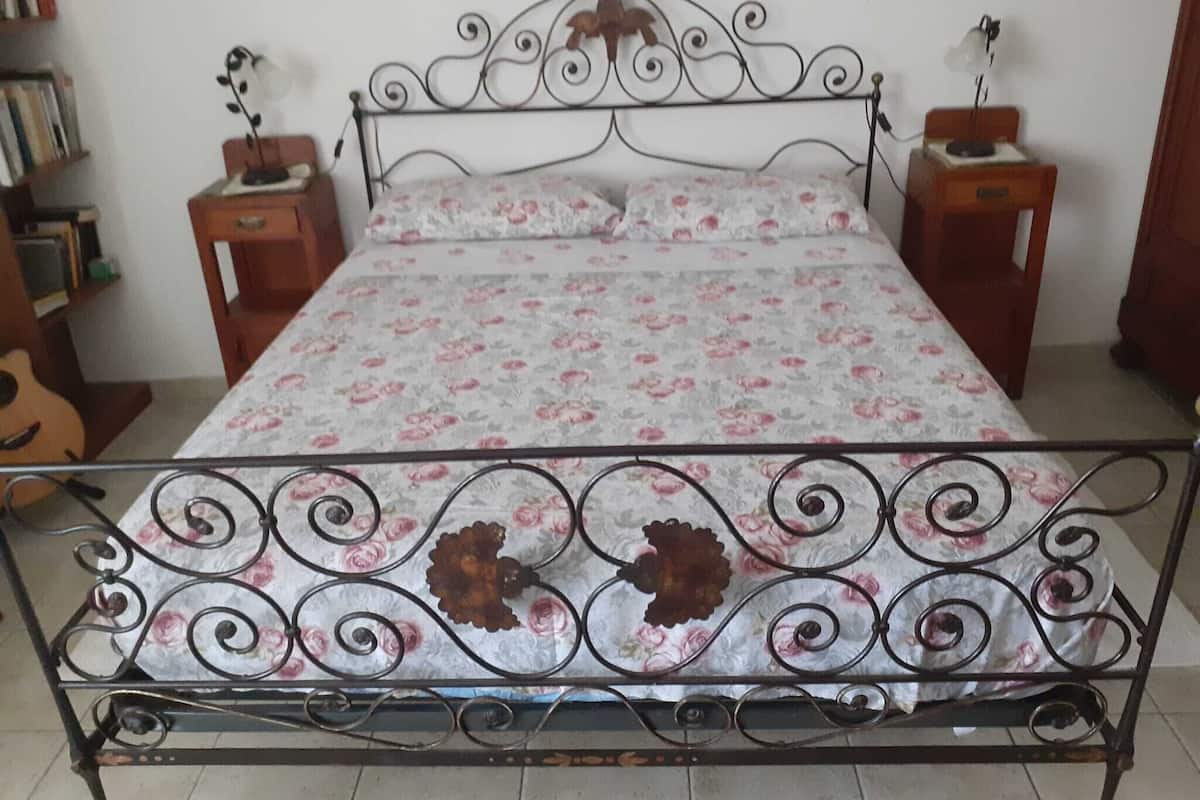 A bed with a floral bedspread, two bedside tables with lamps, and a guitar in the corner.