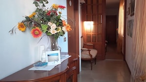 Un pasillo con un escritorio de madera, un jarrón de flores y una silla.