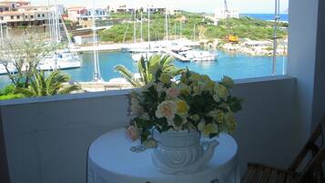 Ein Balkon mit Tisch und Blumenvase, mit Blick auf einen Yachthafen mit Booten und Gebäuden.