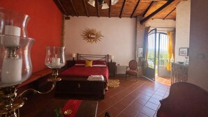 Ein Hotelzimmer mit Bett, Stuhl, Tisch mit Lampe, Sonnendekoration an der Wand und Blick durch eine Tür.