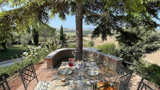 An outdoor dining area with a table set for two, surrounded by greenery and a view of the countryside.