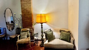 A room with a sofa, a chair, a table, a lamp, a mirror, and a brick wall.