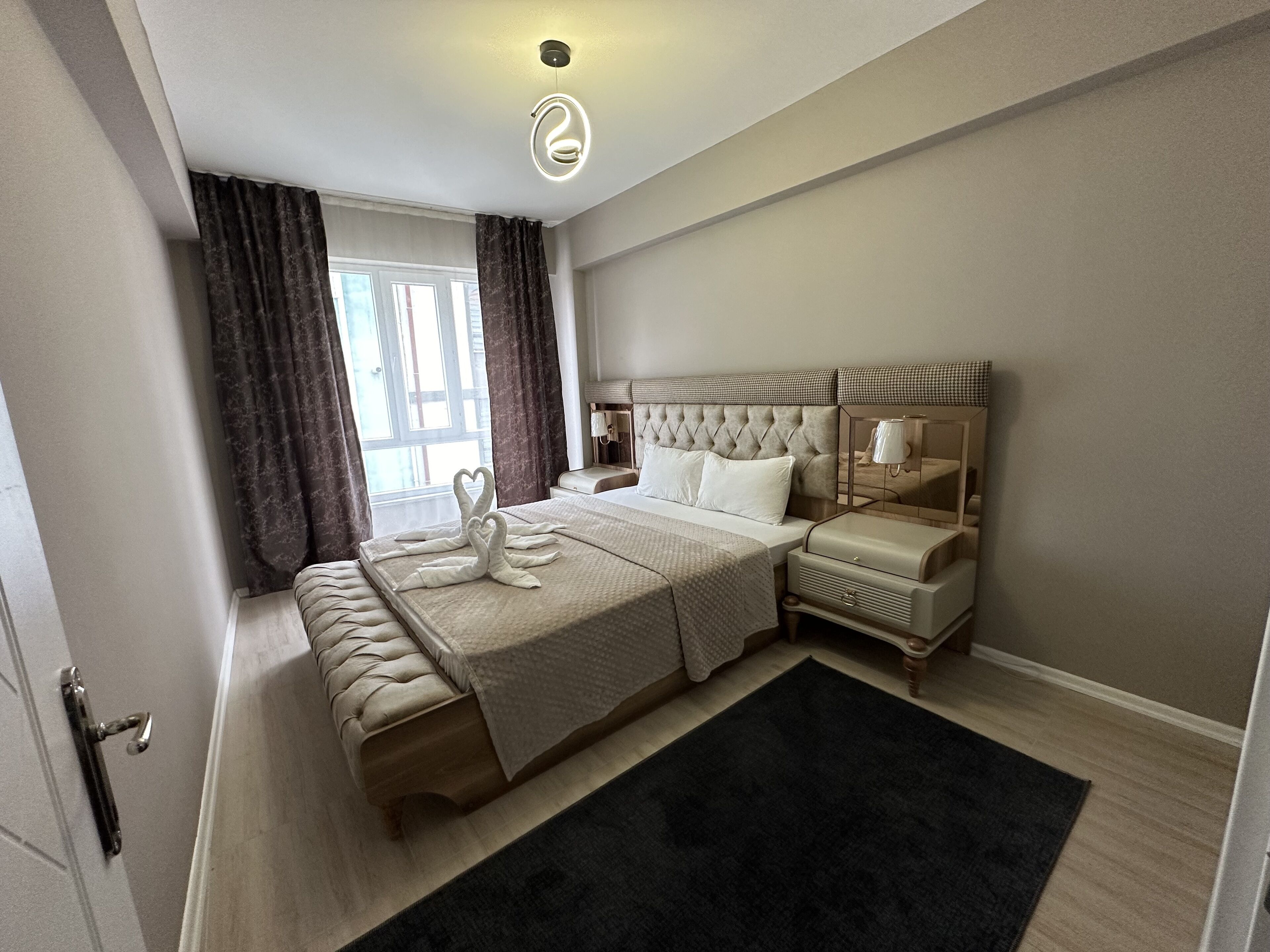 Une chambre d’hôtel moderne avec un grand lit, un banc, une table de chevet et un miroir.