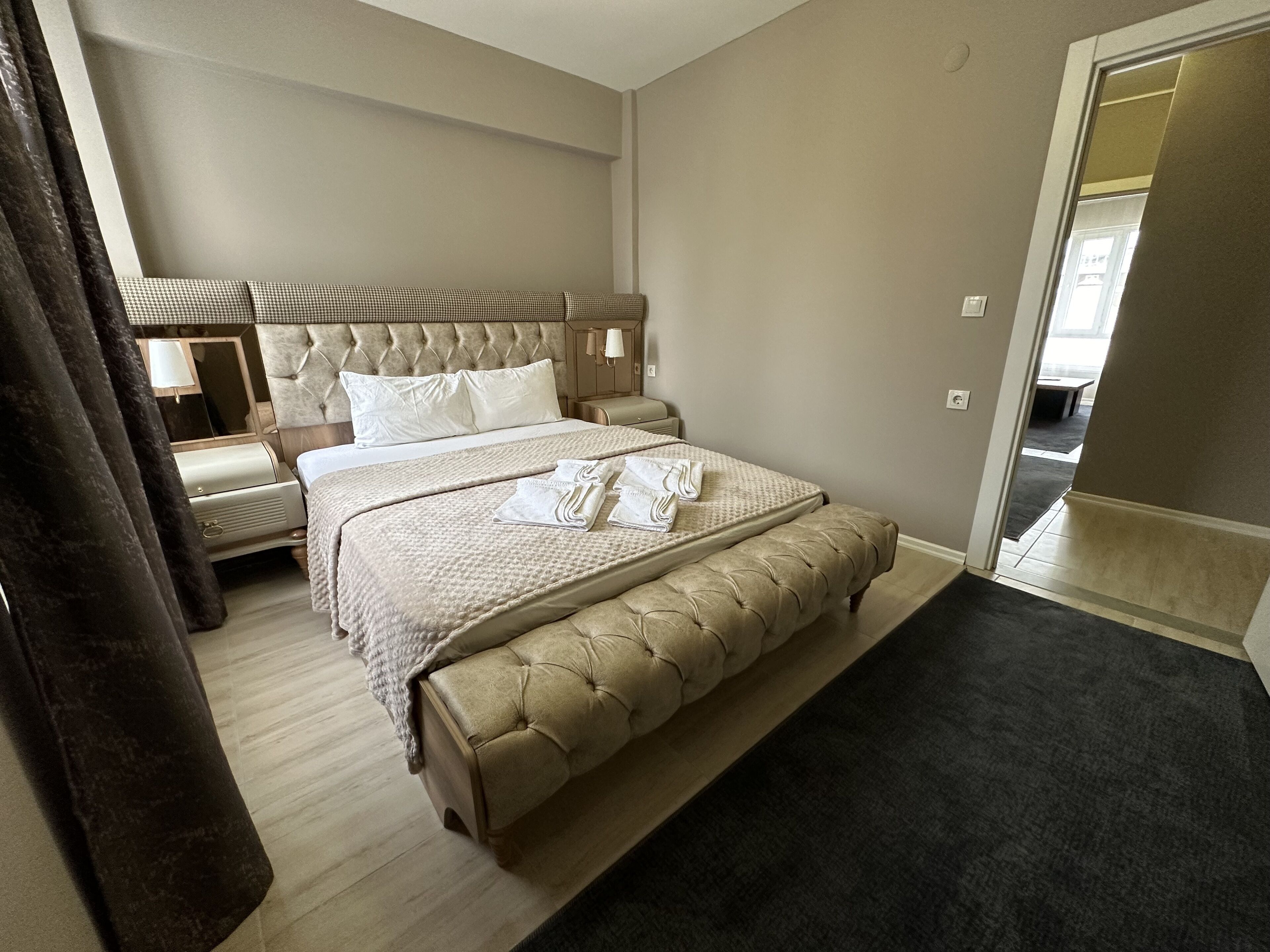 A hotel room with a large bed, a bedside table, a lamp, and a view of the hallway.