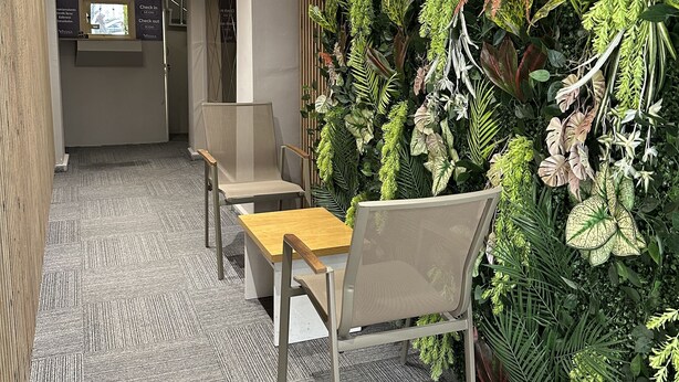 A modern interior with a seating area, a check-in counter, and a wall adorned with artificial greenery.