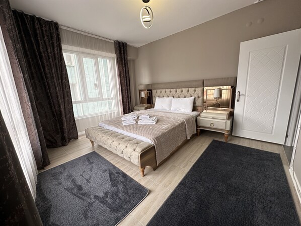 A bedroom with a large bed, a bedside table, a wardrobe, and a window with curtains.