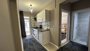 A modern kitchen with white cabinets, a black countertop, and a built-in oven. There is a door leading to a bedroom with a bed and a bathroom with a shower.