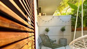 A patio with a wooden slatted wall, a hanging macrame chair, a metal chair, and a small table with two potted plants. - Athenian Coastal Urban Living (Paleo Faliro)