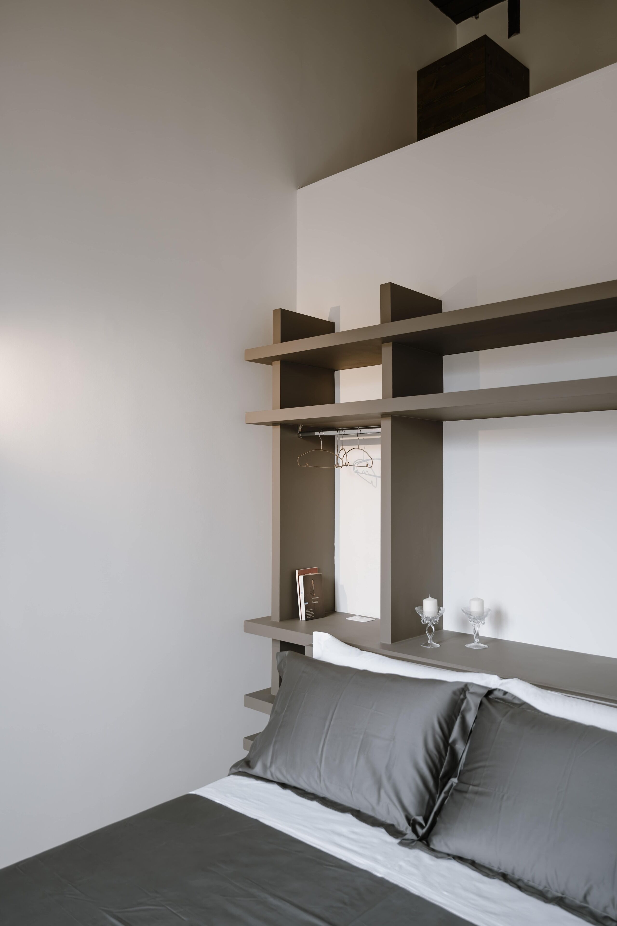 Un dormitorio con cama, almohadas grises, una mesita de noche con vasos y un espejo.