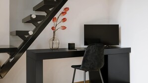 Een moderne kamer met een zwart bureau, een stoel, een flatscreen televisie en een houten vloer.