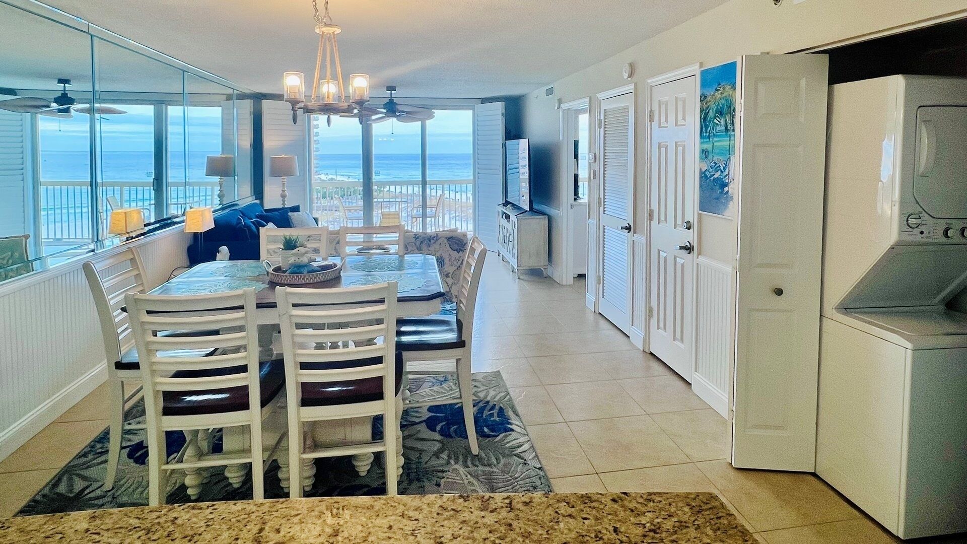A dining area with a view of the ocean, a chandelier, and a kitchen with white cabinets.
