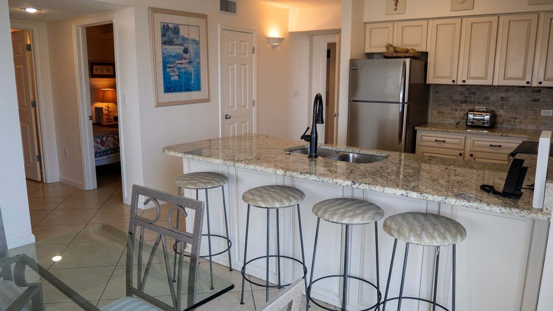 A kitchen with a granite countertop, stainless steel refrigerator, and bar stools.