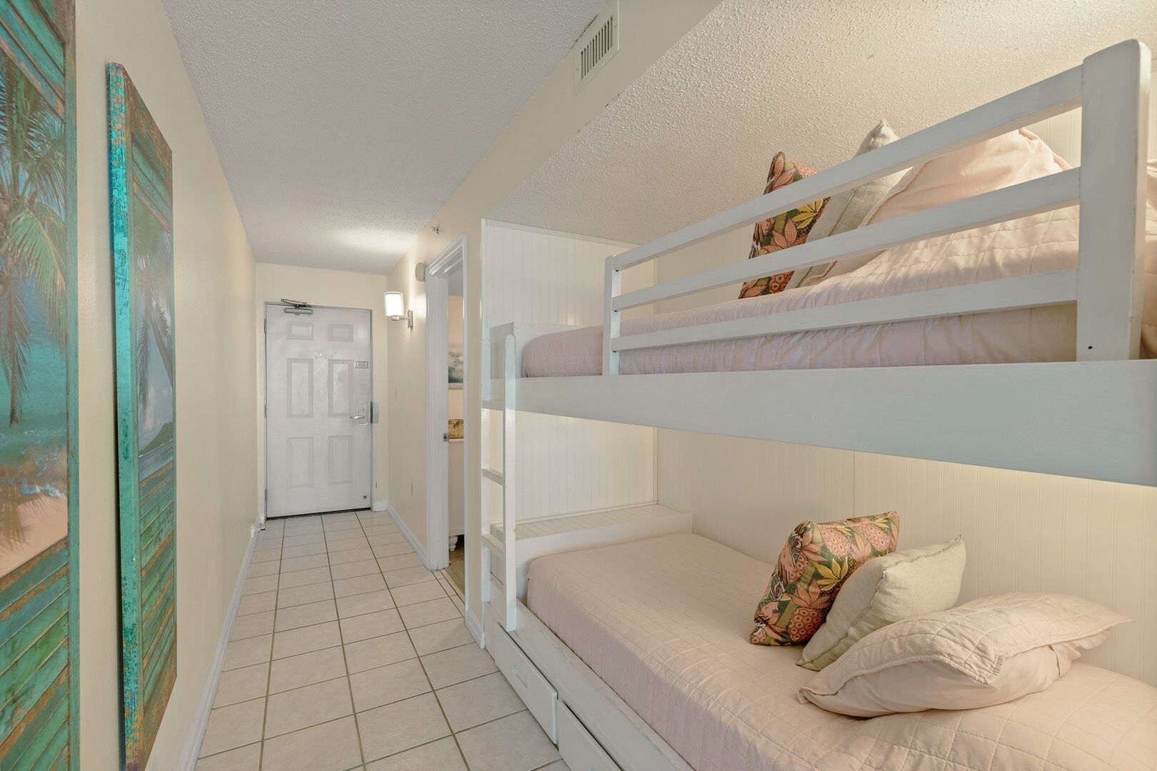 Une chambre avec un lit superposé, une porte, un couloir et un mur orné d’une fresque aux motifs tropicaux.