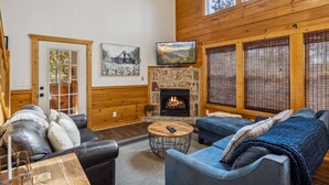 A cozy living room with a fireplace, wooden walls, and a television. - Blue Hawk Hideaway 3 Bedroom Cabin by RedAwning (Sevierville)