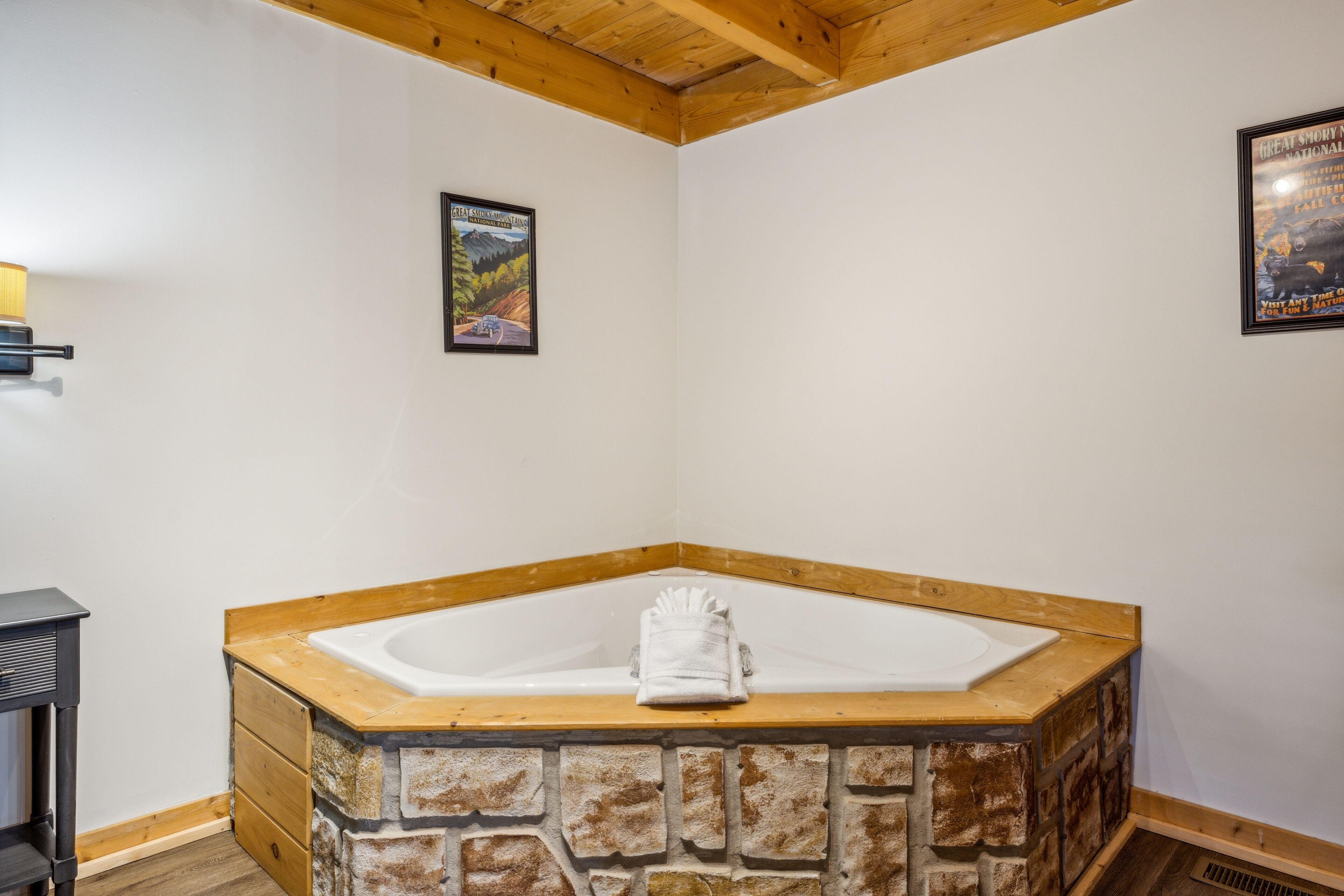 A corner bathroom with a stone wall, a wooden ceiling, and a bathtub.