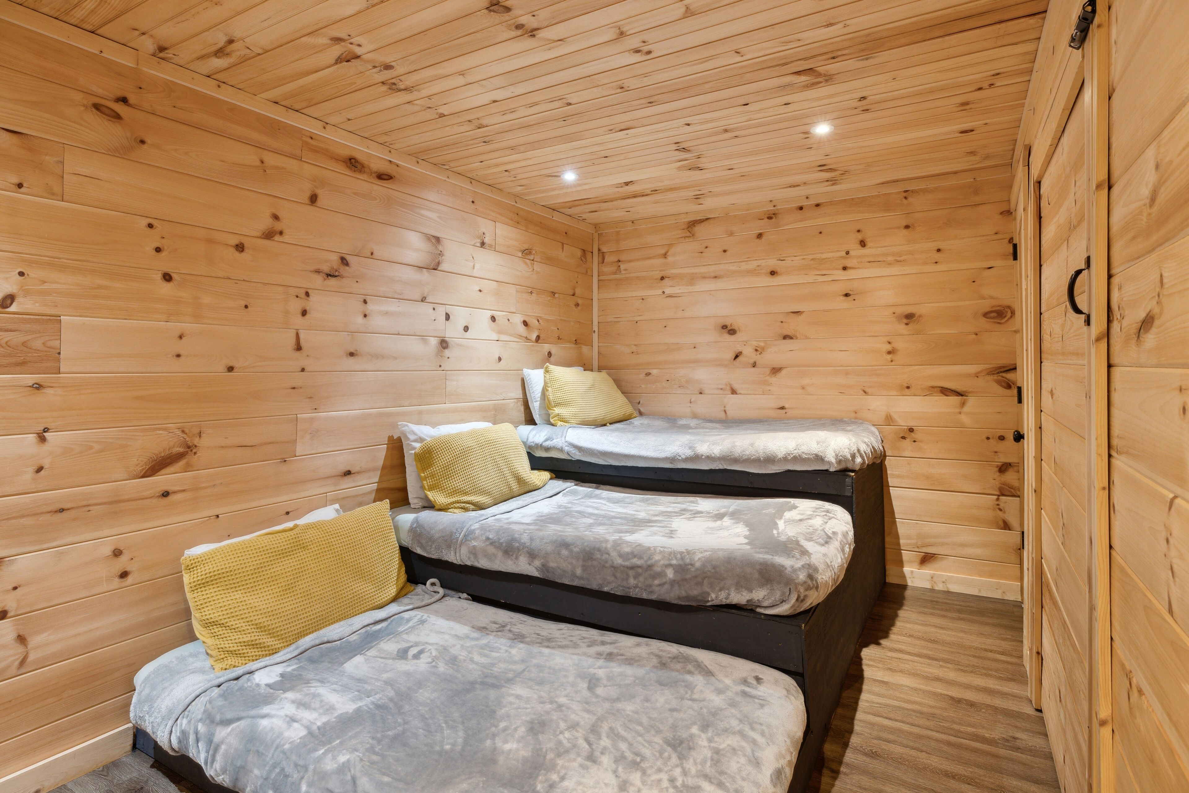 Una cabaña de madera con tres camas, cada una con almohada y manta.