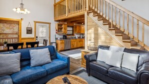 A spacious living area with a blue sofa, a black leather sofa, a wooden coffee table, and a wooden staircase leading to an upper level. - Blue Hawk Hideaway 3 Bedroom Cabin by RedAwning (Sevierville)