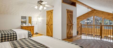 A bedroom with two beds, wooden beams, a ceiling fan, and large windows.