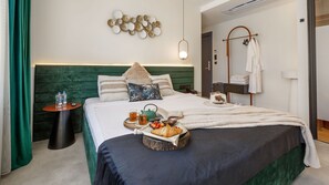 Un lit bien fait, avec un plateau contenant des articles pour le petit-déjeuner, une table de chevet avec une lampe, une œuvre d’art accrochée au mur et un porte-peignoir.